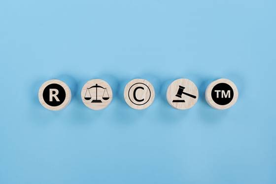 Five wooden discs, arranged linearly, symbolize legal protections: (R) Registered trademark, scales of justice, (C) Copyright, a gavel, and (TM) Trademark. This represents the importance of intellectual property rights.